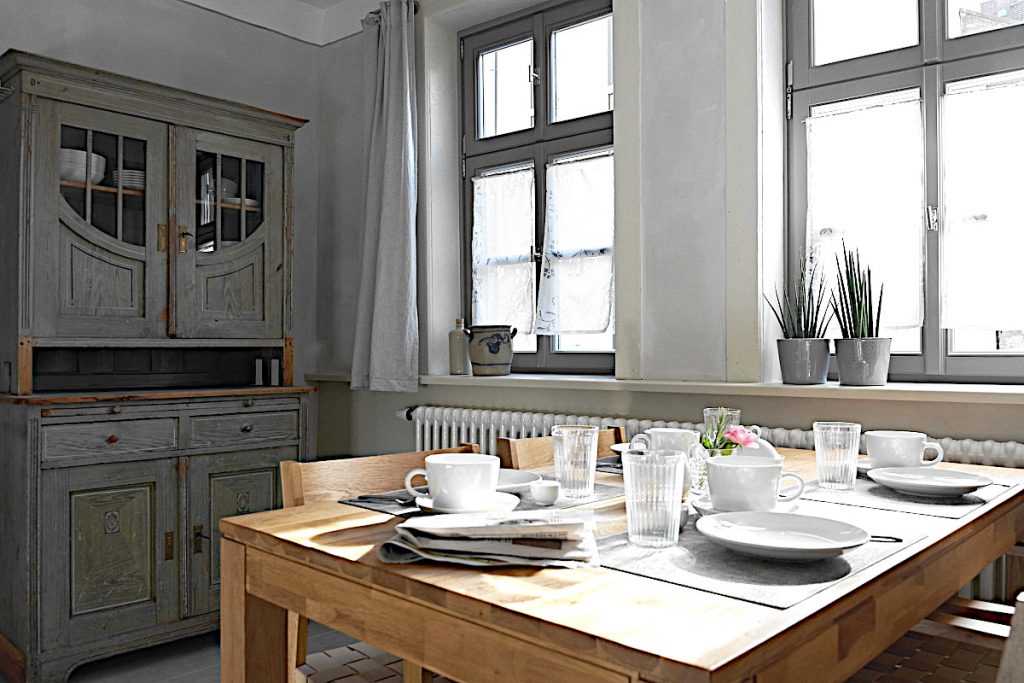 Brauner Holz - Esstisch in der Küche eingedeckt mit weißem Geschirr und Geschirrschrank.