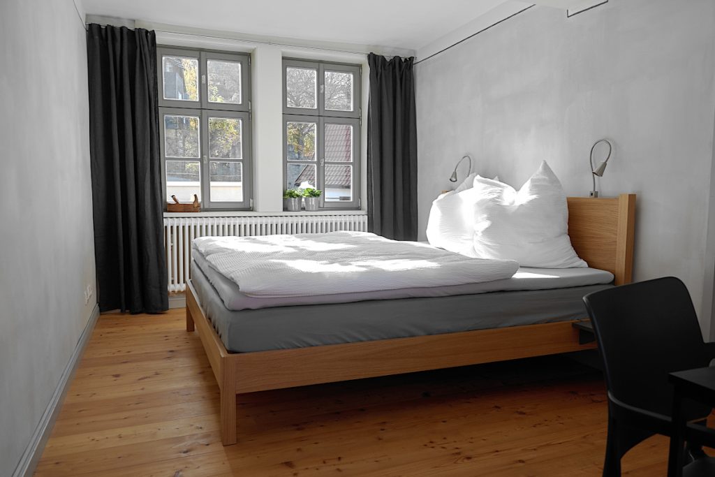 Grau gestrichenes Schlafzimmer mit großem Doppelbett aus braunem Holz mit weißer Bettwäsche.