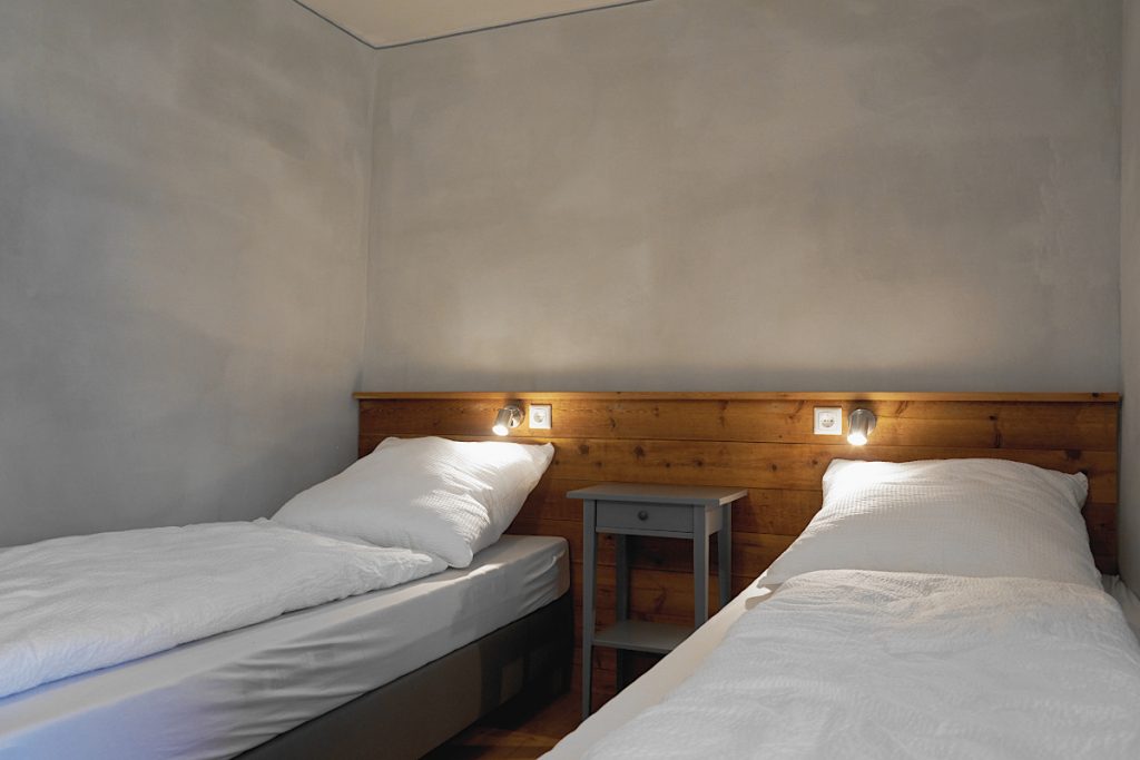 Grau gestrichenes Schlafzimmer mit zwei Einzelbetten und Holzverkleidung am Kopfende.