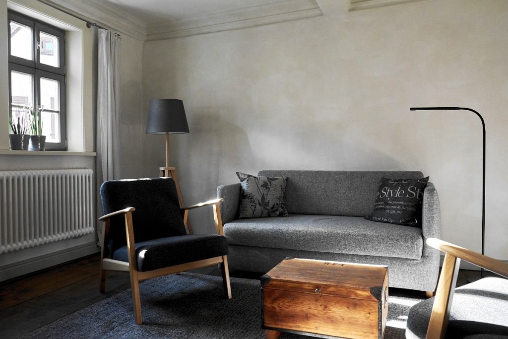 Grau gestrichenes Wohnzimmer mit grauem Schlafsofa und zwei Sesseln.