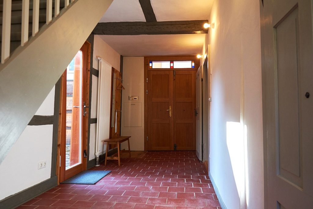 Das Ferienhaus, Flur im Erdgeschoss mit Eingangstür, Garderobe und einem Fußboden aus roten Ziegelplatten.