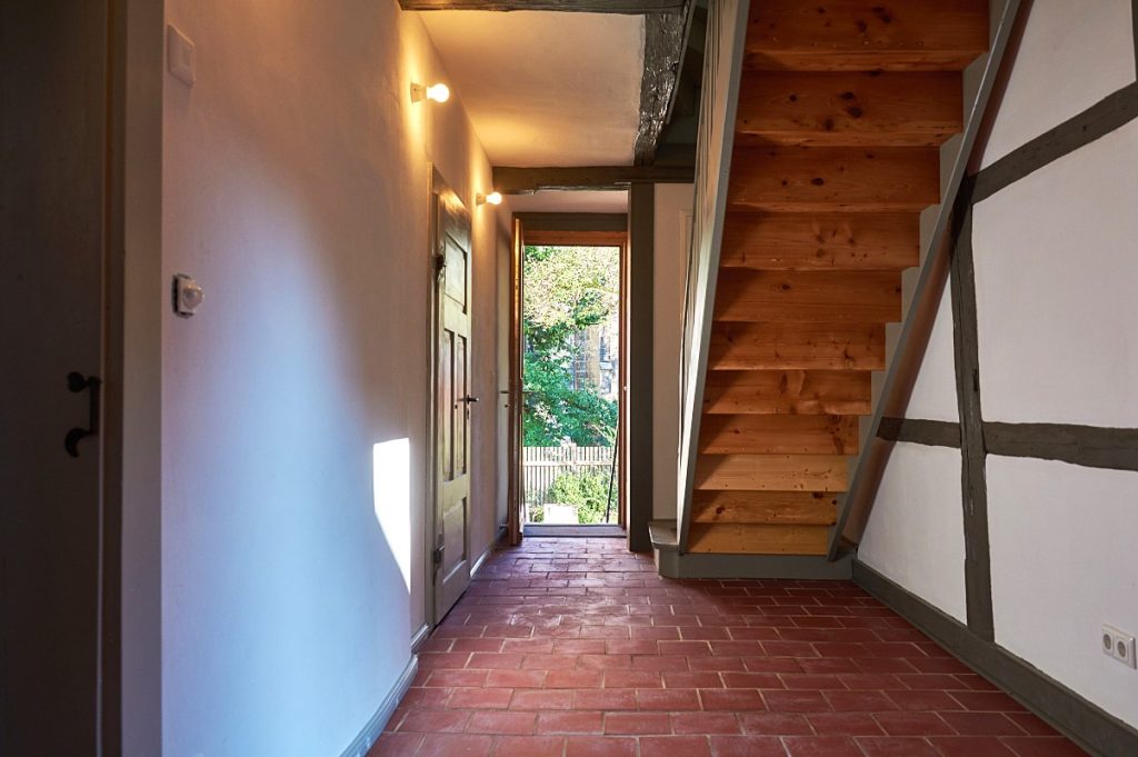 Das Ferienhaus, Flur im Erdgeschoss mit Holztreppe nach oben und einem Fußboden aus roten Ziegelplatten.