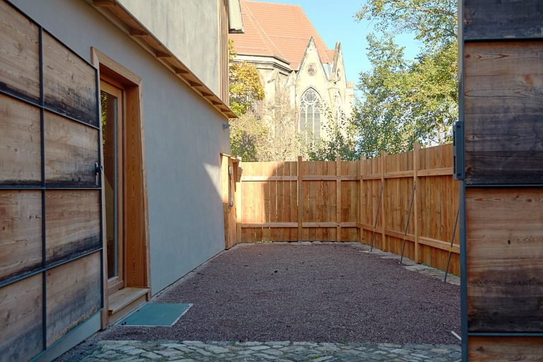 Das Ferienhaus, Parkplatz bestreut mit feinem Kies und eingefasst mit einem braunen Bretterzaun aus Lärche.