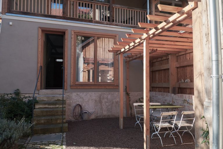 Das Ferienhaus, Sitzplatz im Hof unter einer Pergola bestreut mit feinem Kies.