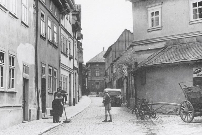Alte Ansicht der Mittelgasse mit altem Auto, Pferdewagen und Menschen auf der Straße.