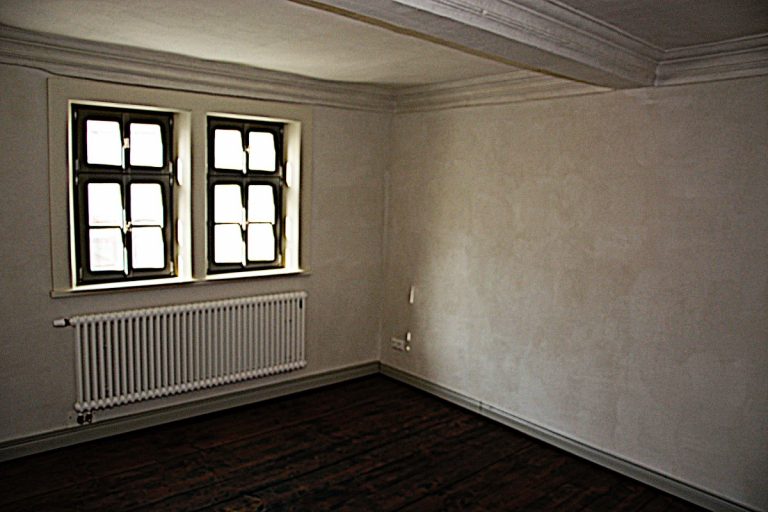 Ferienhaus Mittelgasse 15, Wohnzimmer mit hellgrau gestrichenen Wänden, dunkelbraunen Holzdielen und grauen Scheuerleisten.