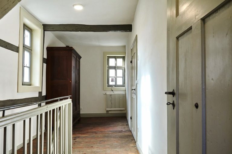 Alte Türen, Treppen, Geländer im Flur verschieden grau gestrichen, der Dielenfußboden braun geölt.